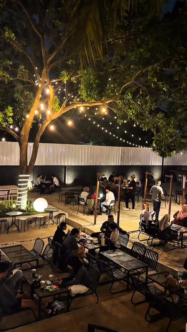 Area outdoor EFORIUM pada malam hari dengan lampu gantung di pohon dan tamu yang memenuhi meja